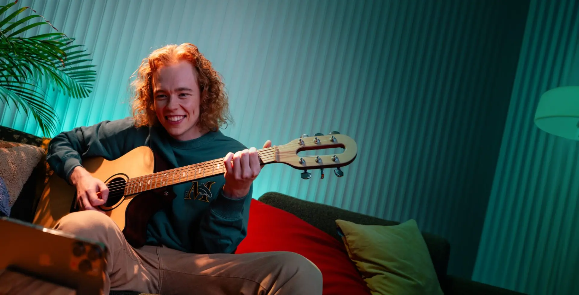 A person playing an acoustic guitar on a sofa
